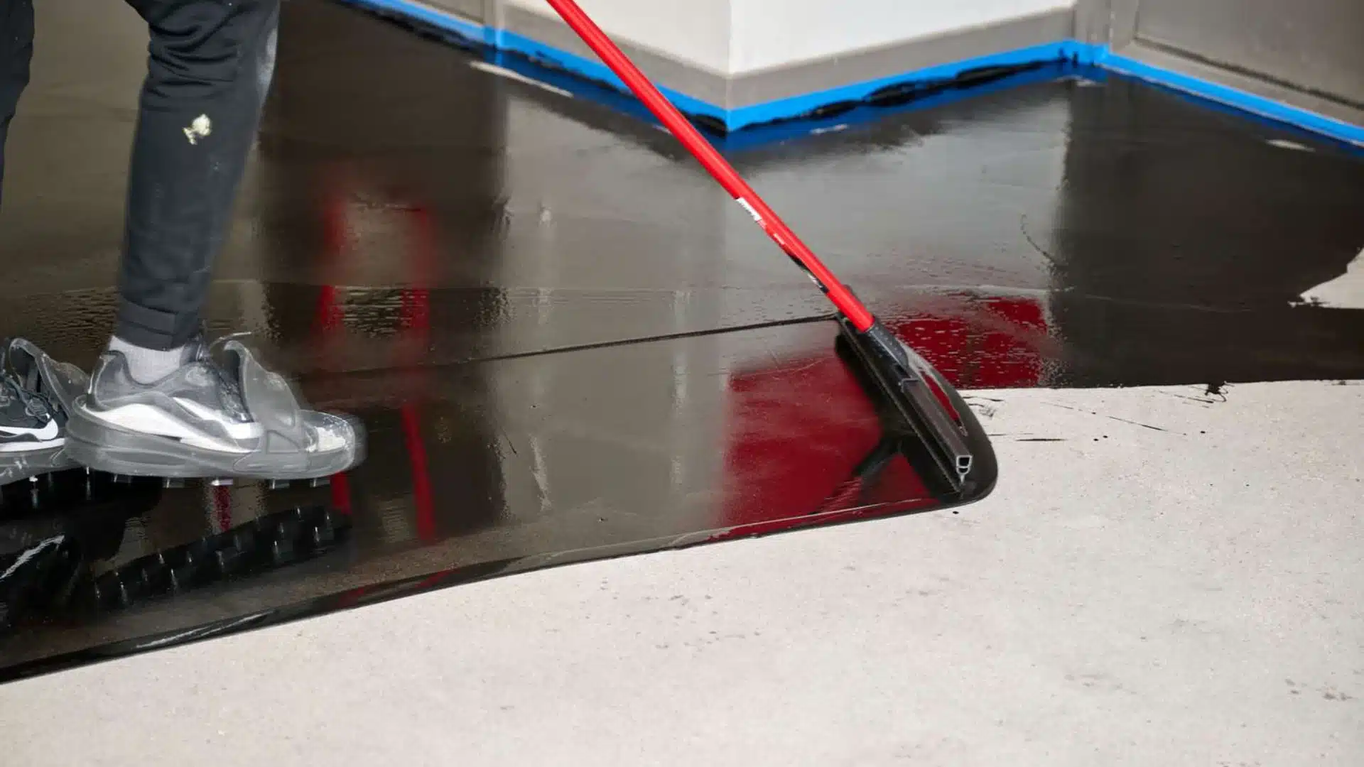 A person applying the first coat of epoxy on the garage floor using a roller