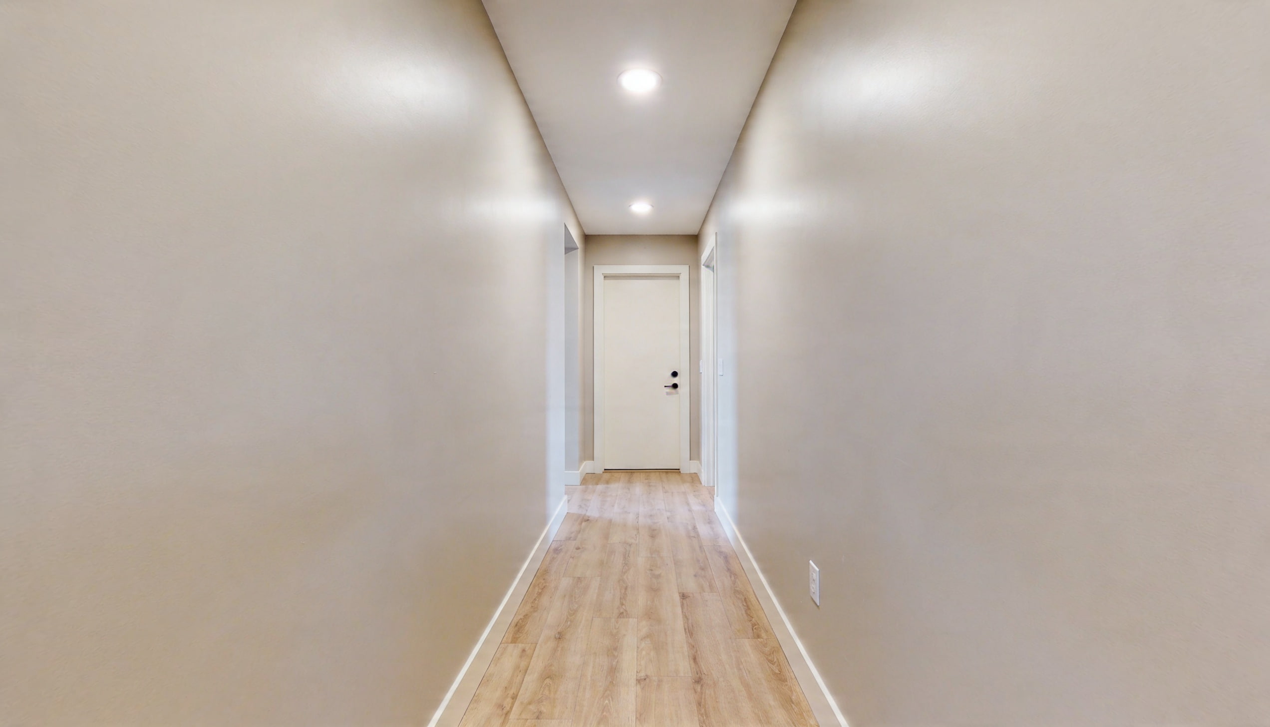 A spacious hallway with a door at the far end, bathed in warm light.