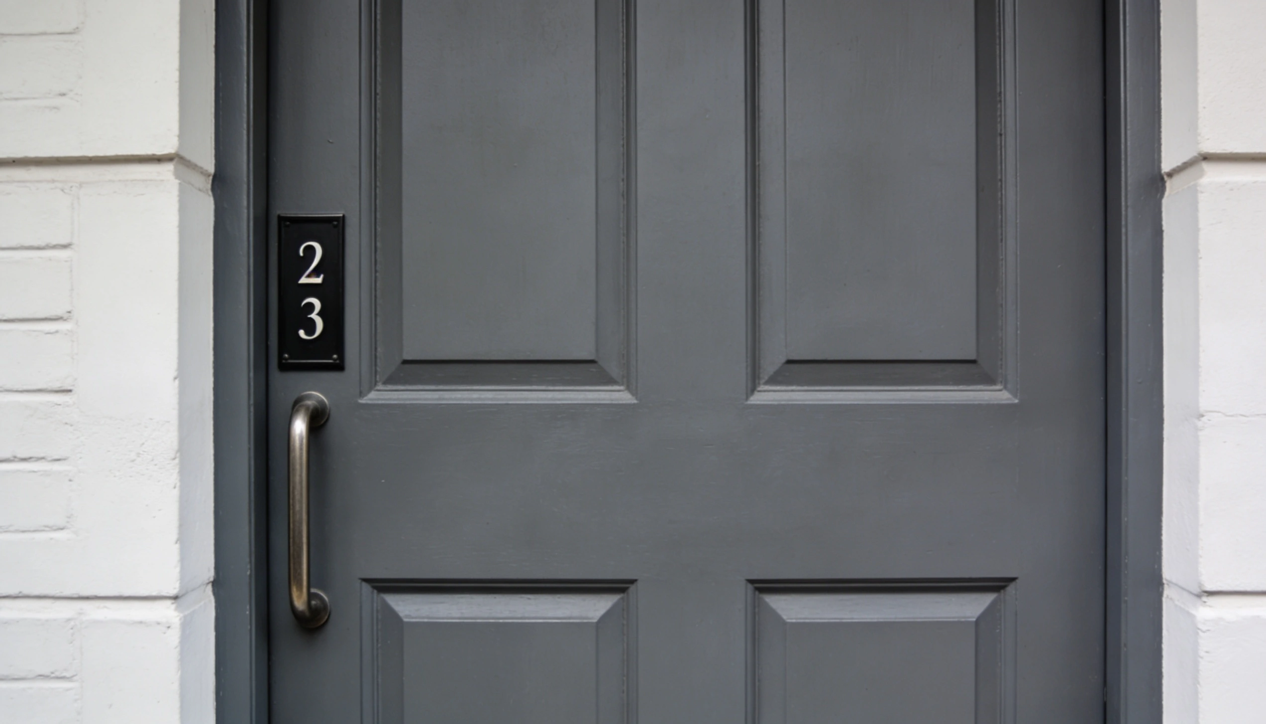 Charcoal grey front door with panel design and metal handle, set in white brick exterior, showing modern home entrance design